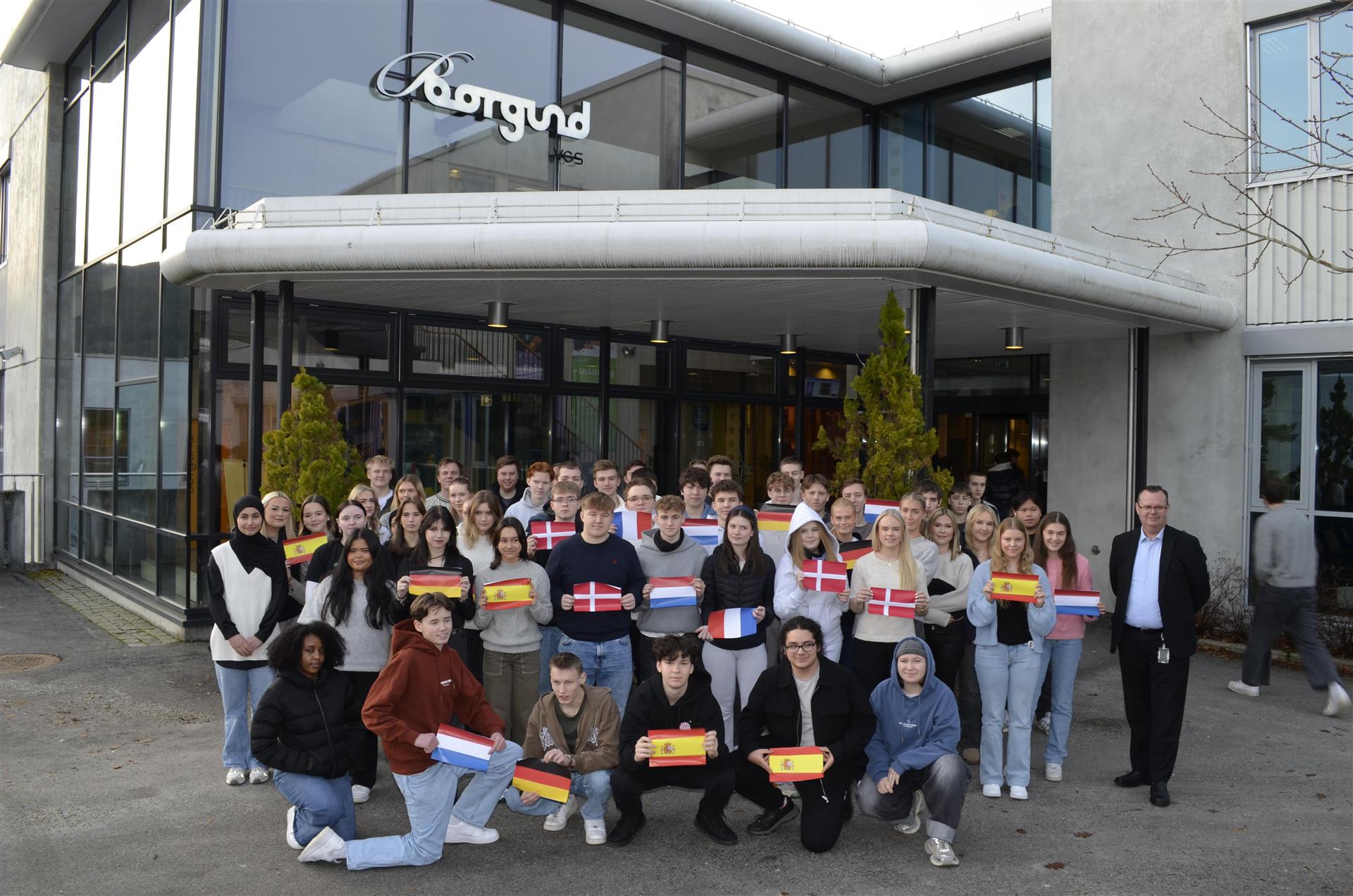 Bilde av elever med ulike flagg oppstil foran hovedinngang til skolen