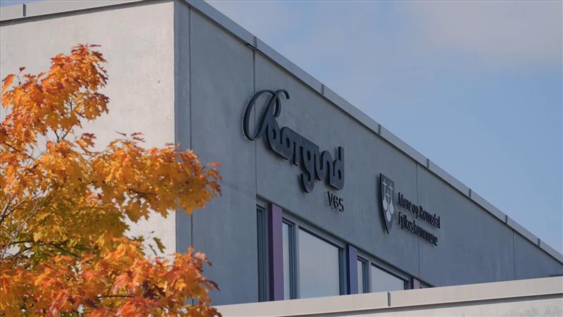 Foto av skolebygg med logo til skolen. Trær i høstfarger